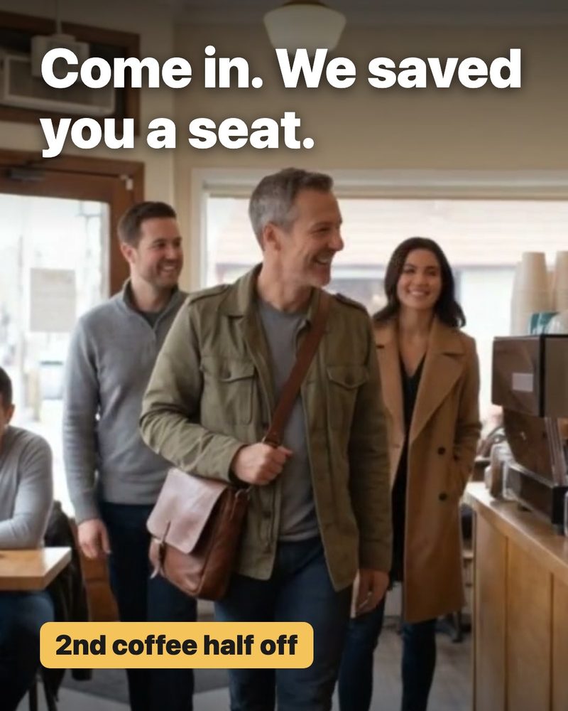 Customers walking into a busy cafe past the counter, with the words Come in. We saved you a seat. and the badge 2nd coffee half off on it (sample)